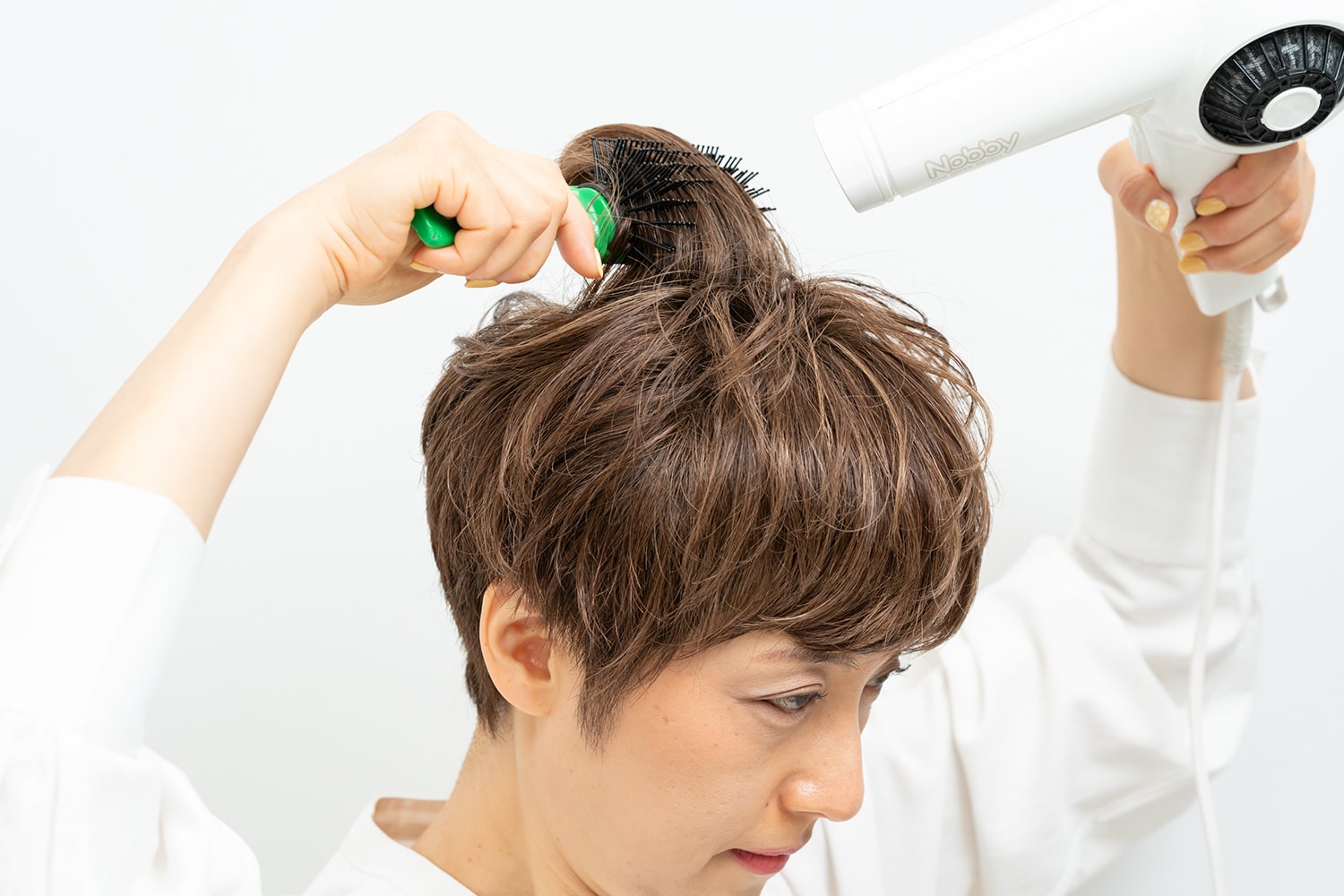 ブラシでつむじ周りの髪をざっくりと取って根元に熱風を当てる。