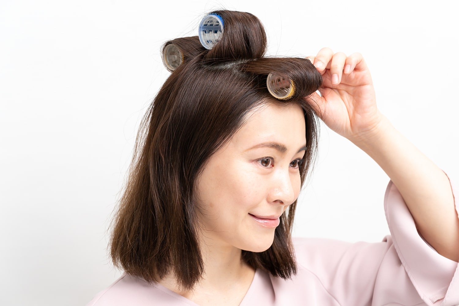 毛束を頭皮に対して垂直に引き上げた状態で毛先からカーラーに巻き付ける。中央と後頭部のカーラーは後頭部方向に、前髪は顔方向に巻き付ける。
