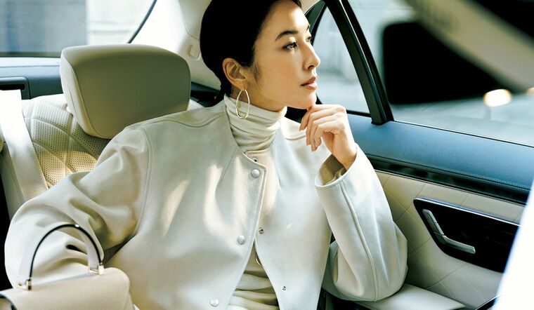 自動車内に座る、ホワイトのジャケットとニット、パンツを着用したモデル