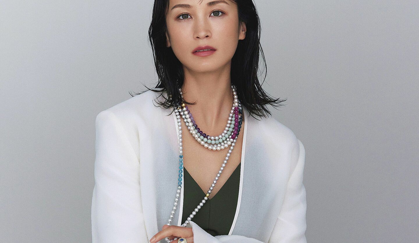 黒田エイミさんが白のジャケットにカーキのオールインワンを着てパールやカラーストーンのネックレスを纏った写真
