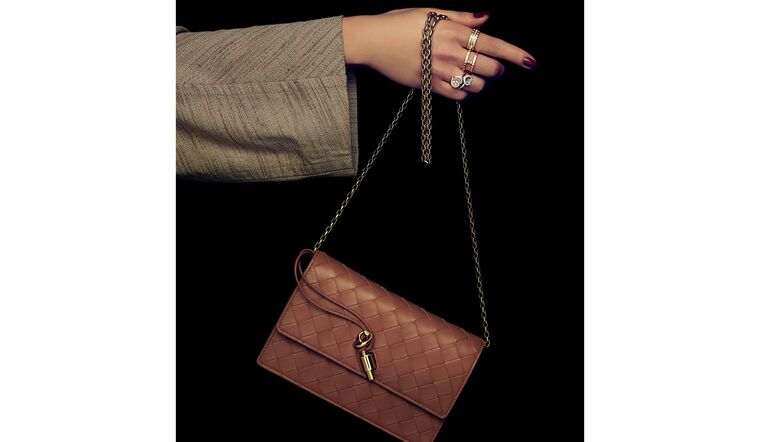 「ボッテガ・ヴェネタ」のウォレットバッグと「ショパール」のジュエリーを纏った女性の手元