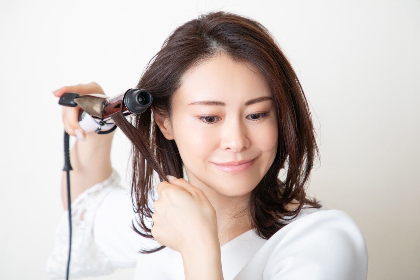 最後に、こめかみ付近の毛束を取って中間をコテで挟む。毛先を持って、コテを外側に引っ張るように当ててカールをつける。
