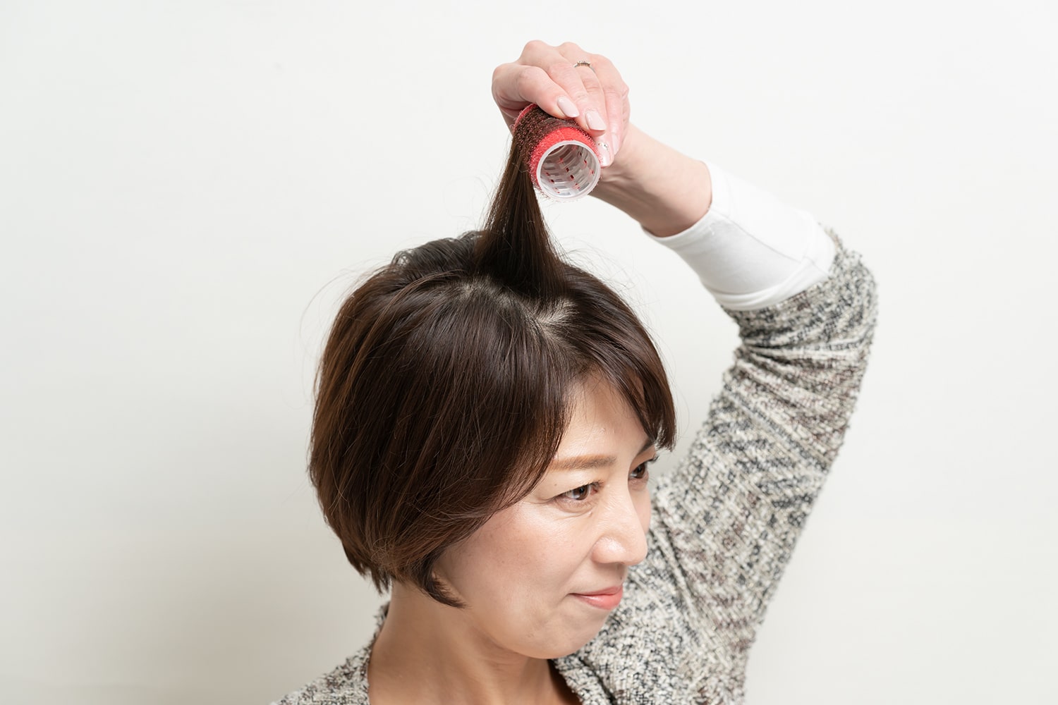 毛束を頭皮に対して90度になるように持ち上げ、縦向きにしたカーラーに毛先から巻く。