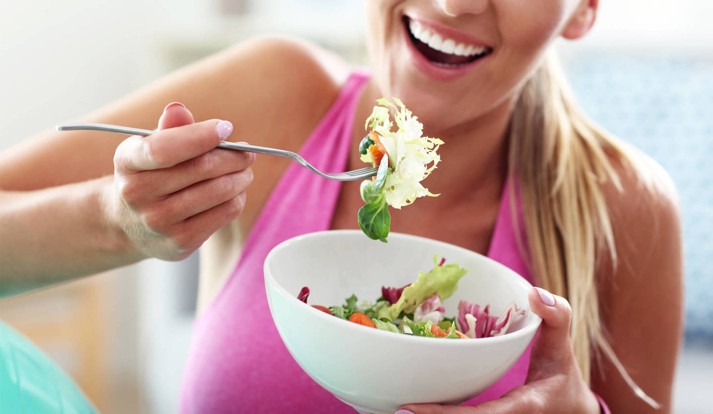 ダイエットをしているピンク色のタンクトップを着た女性がサラダを食べようとしている様子